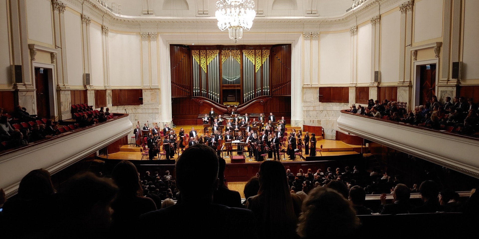 sala Filharmonii Narodowej, na scenie orkiestra, białe balkony, dużo ludzi na widowni